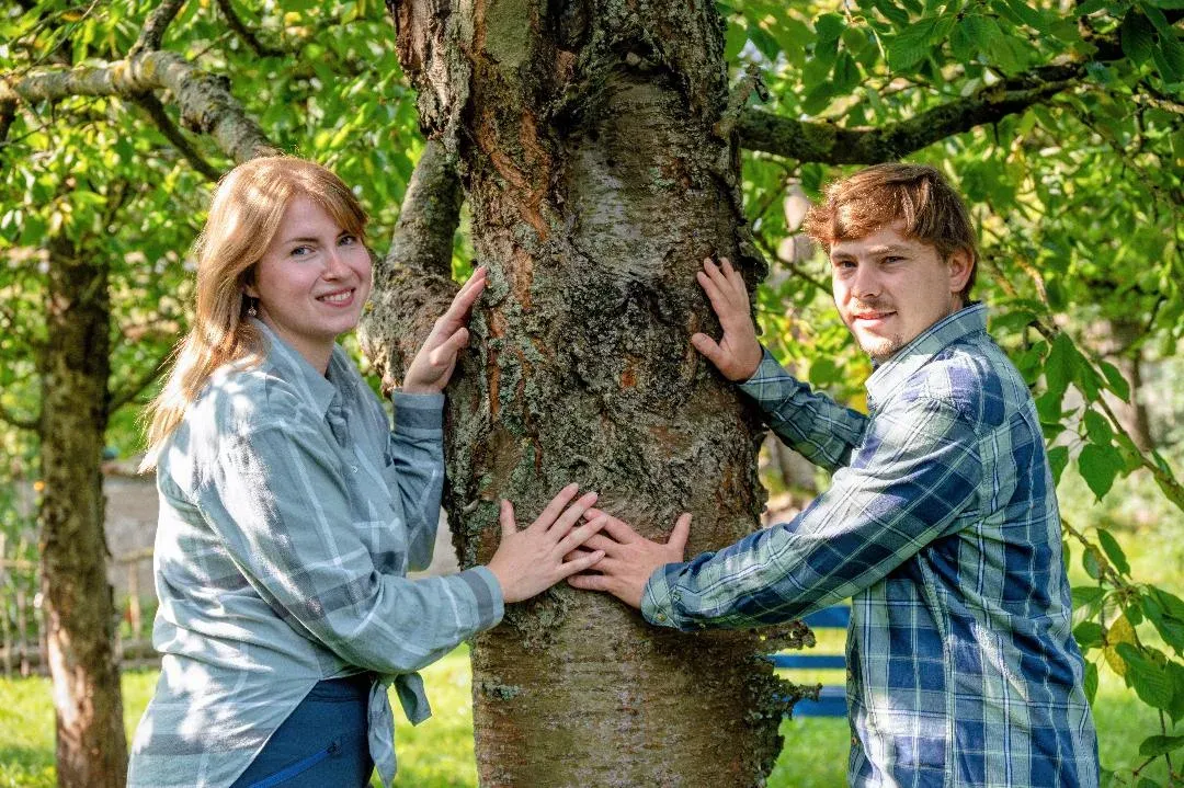 Paula und Jonas lehnen lächelnd an einem Obstbaum