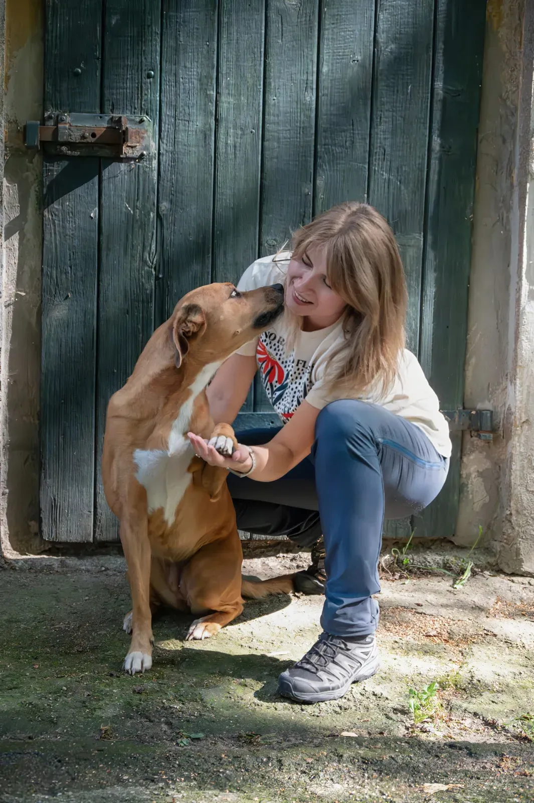 Paula kuschelt vor einer alten Holztür auf dem Hof mit ihrem Hund